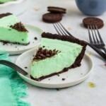 Grasshopper pie in a white pie dish with oreos on the table.