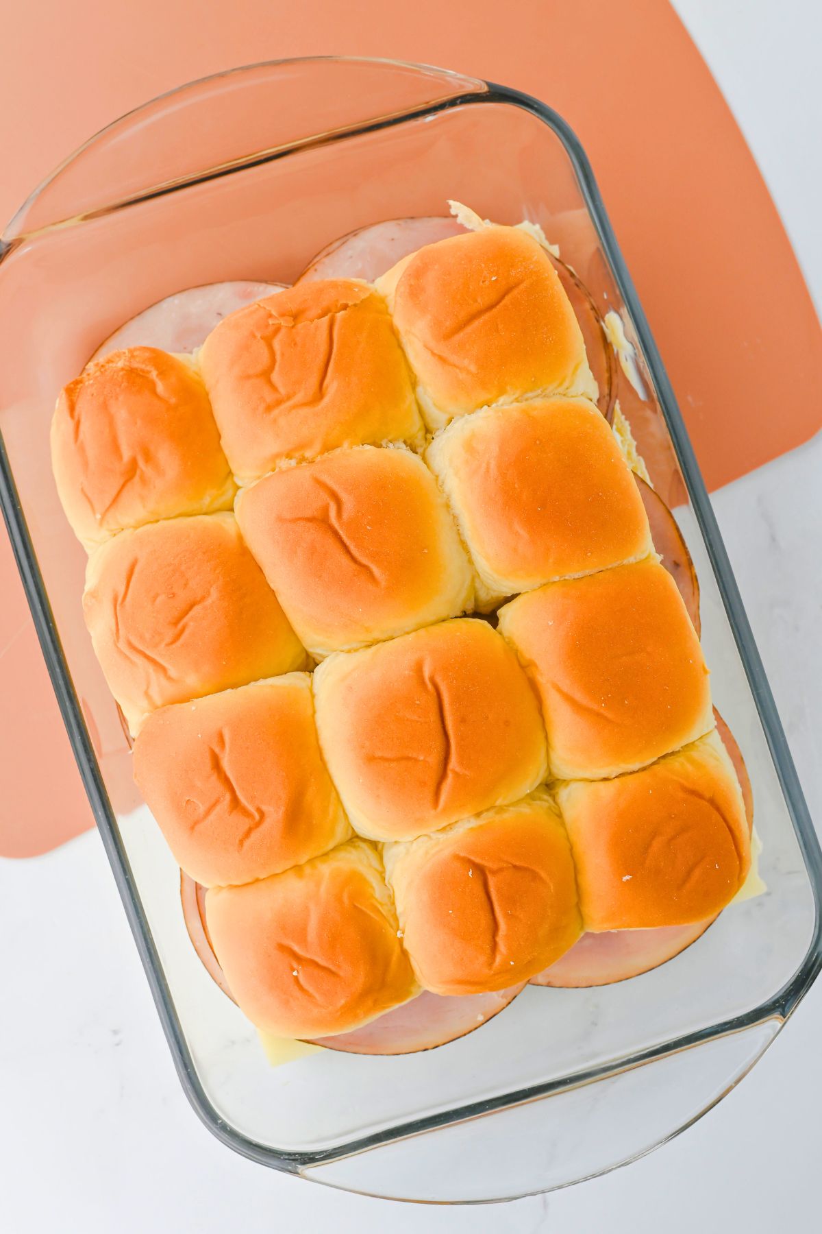 Sliders with ham and cheese in a glass baking dish.