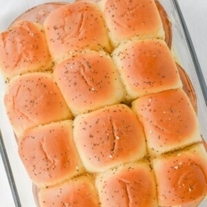 Melted butter with seasonings brushed on top of ham and cheese sliders.