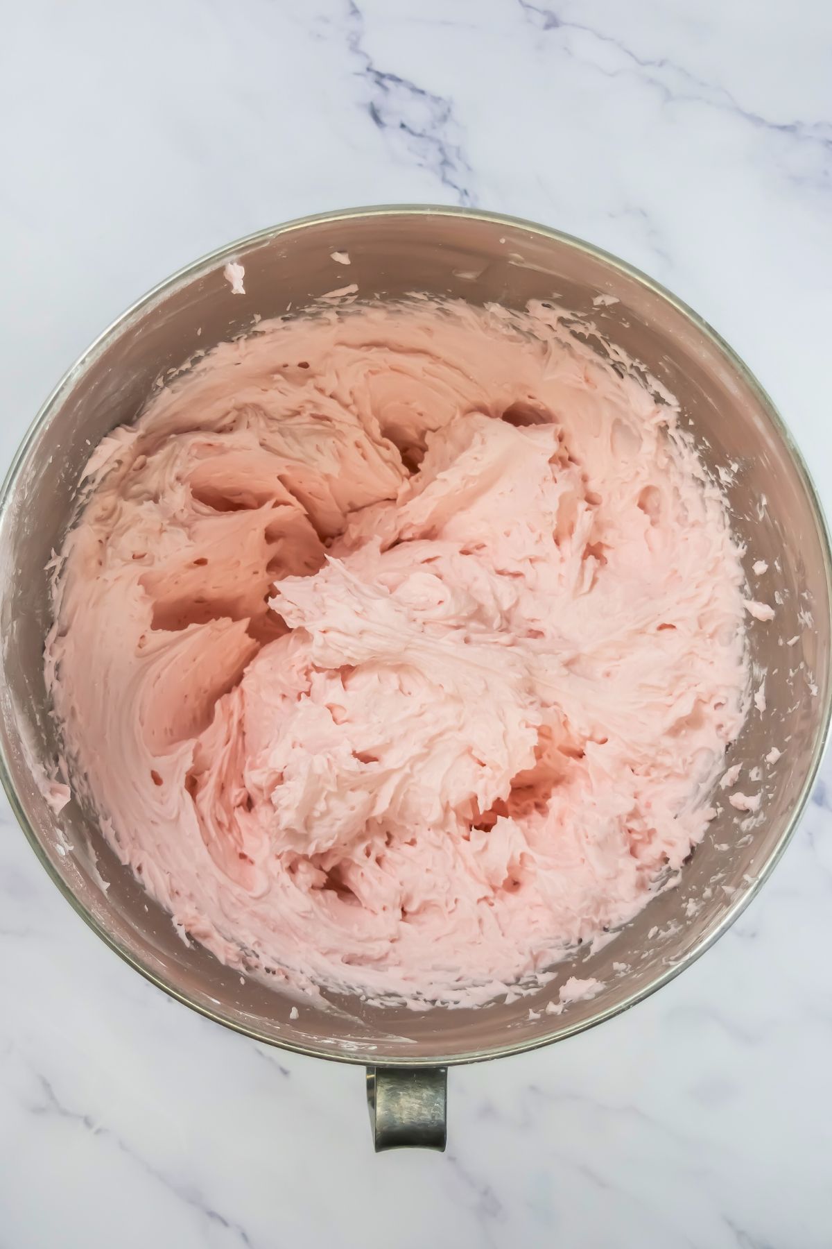 Pink buttercream in a silver mixing bowl. 