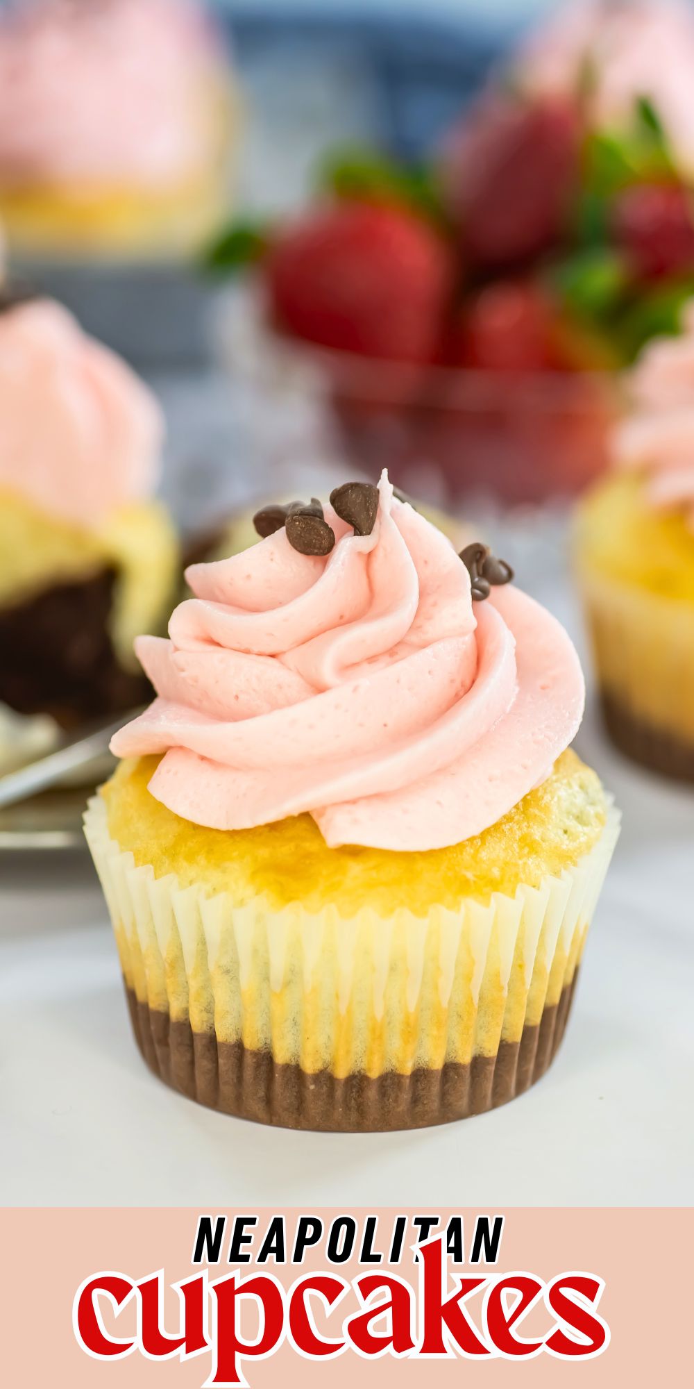 Neapolitan cupcakes with pink frosting on top, in front of a bowl of fresh strawberries.