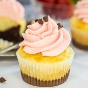 Neapolitan cupcakes with pink frosting on top, in front of a bowl of fresh strawberries.