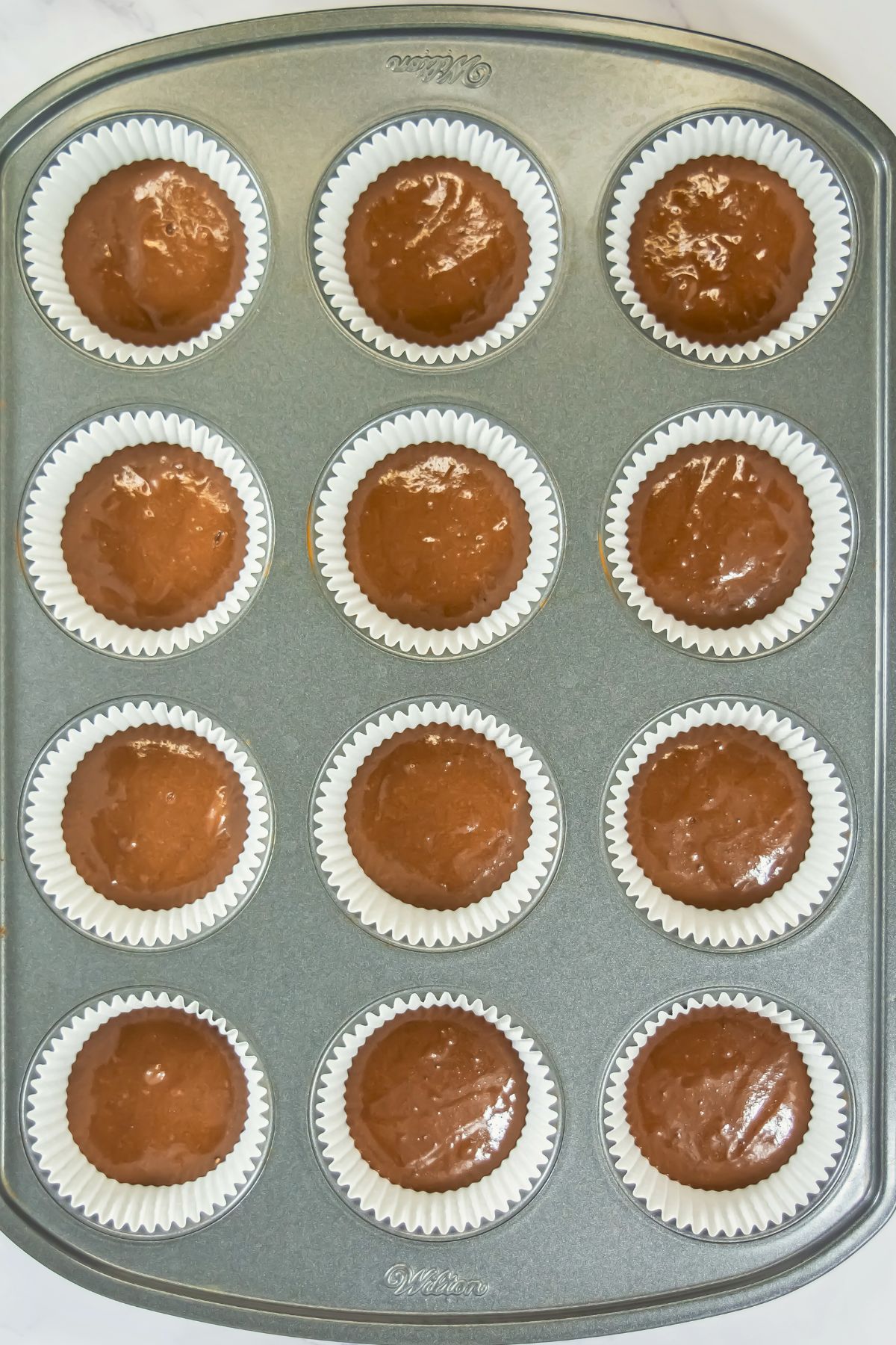 Chocolate cake batter in cupcake liners in a pan before being baked. 
