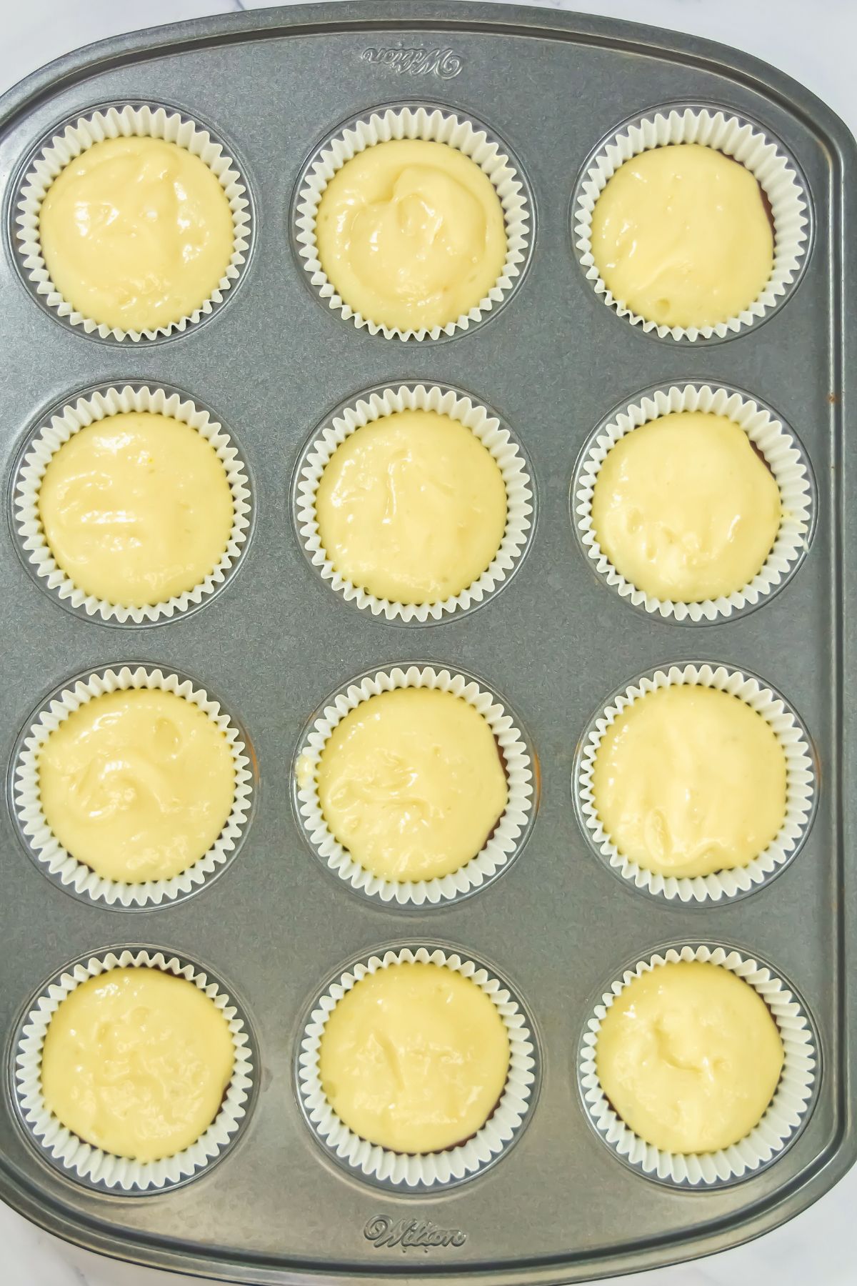 Vanilla cake batter spooned over chocolate cake batter in liners. 