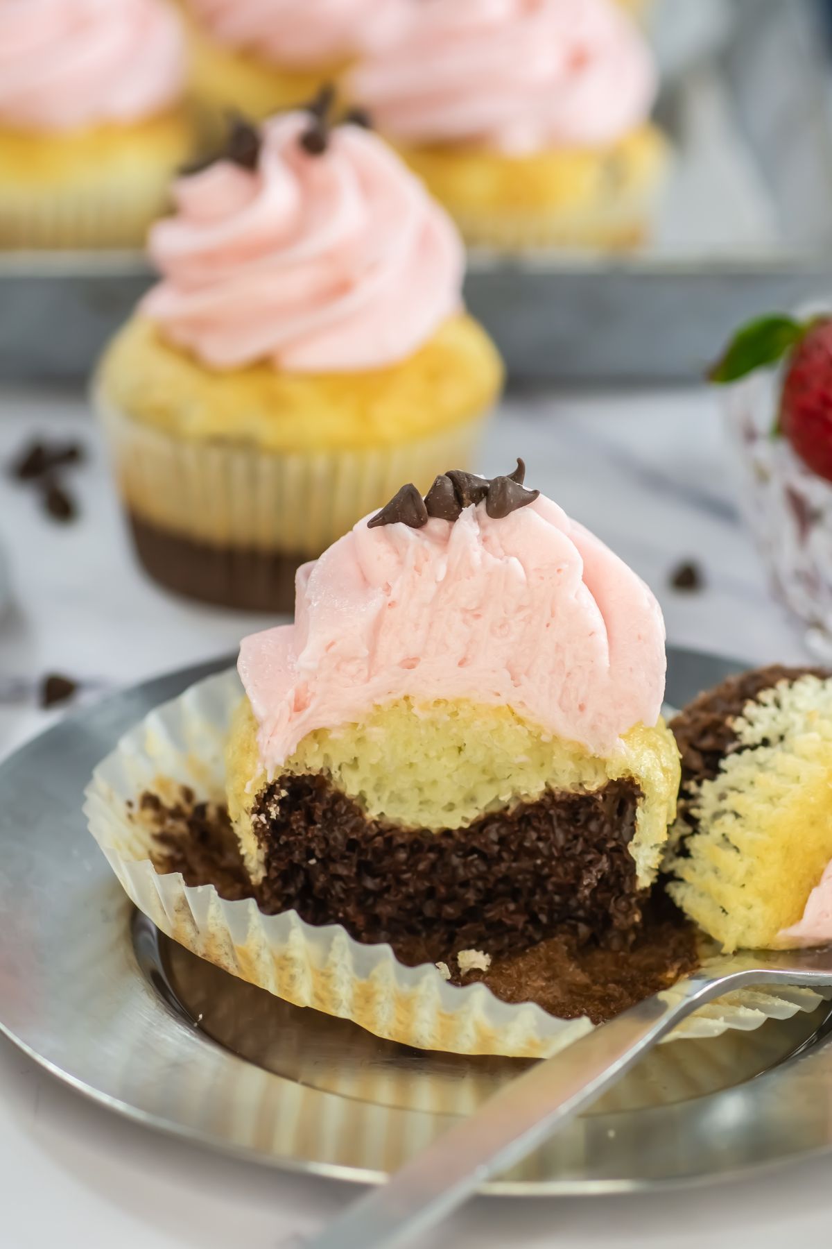 Neapolitan cupcakes with chocolate and vanilla layers, topped with pink frosting, on silver plate. 