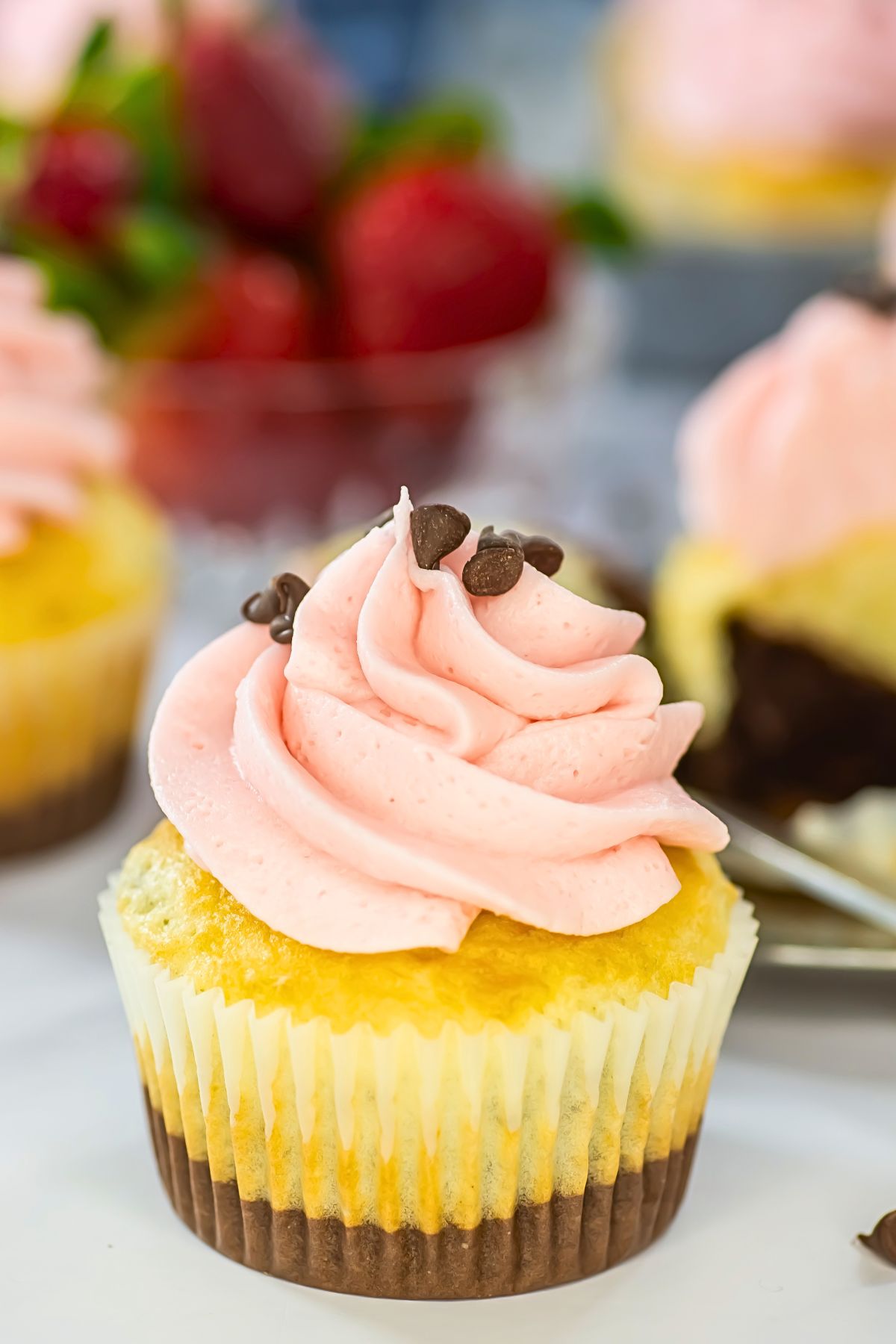 Neapolitan cupcakes with pink frosting on top, in front of a bowl of fresh strawberries. 