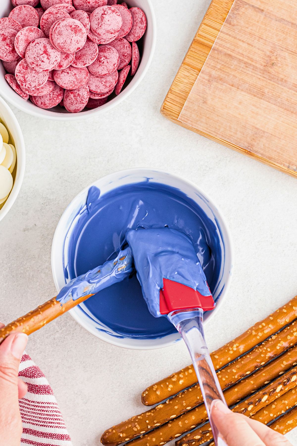 Melted blue candy melts with a pretzel rod being dipped and coated in the blue.