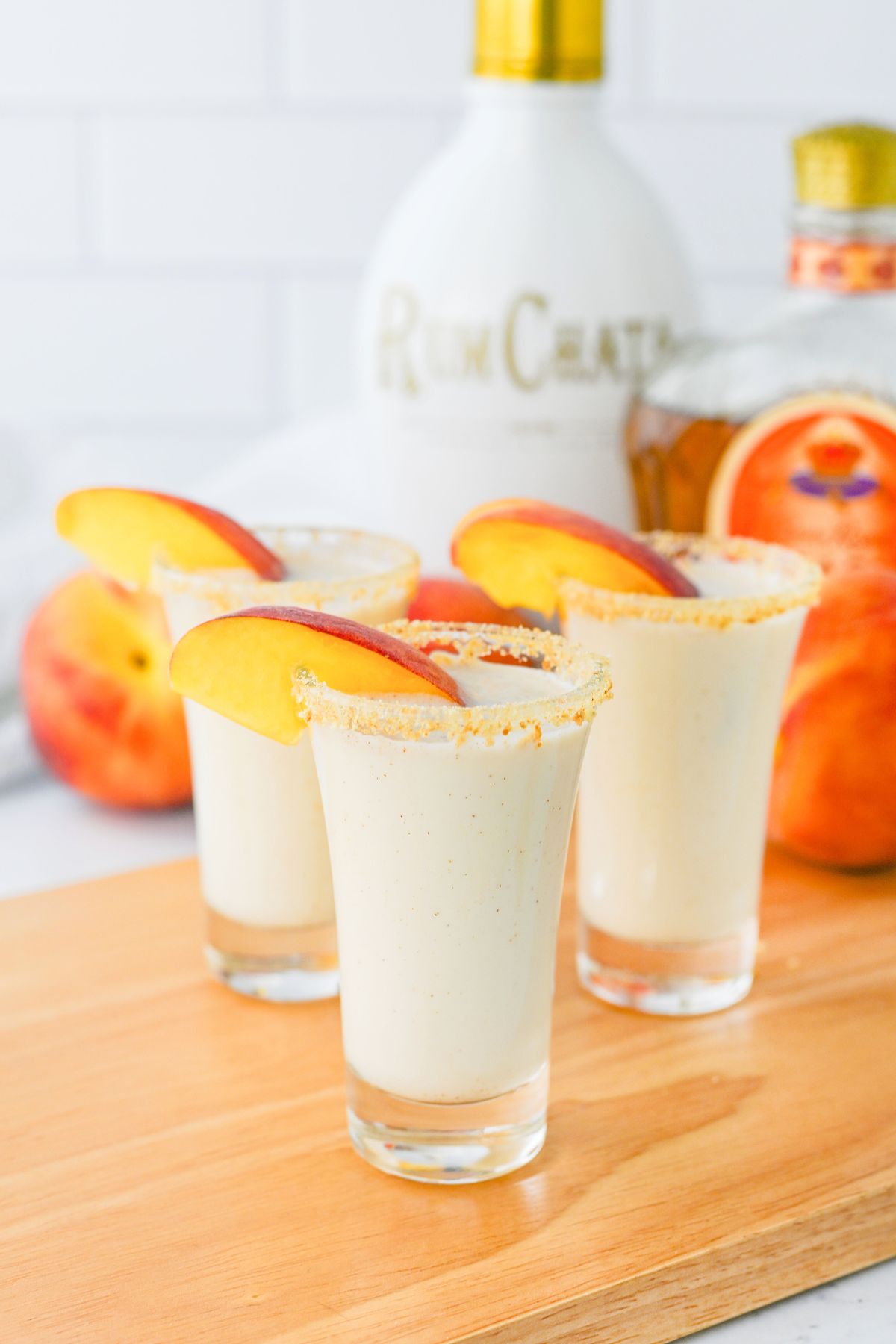 Small shot glass with creamy drink, garnished with a fresh peach slice. 