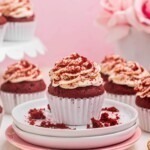 Bright red velvet cupcakes on a small white plate with cupcakes behind the plate.