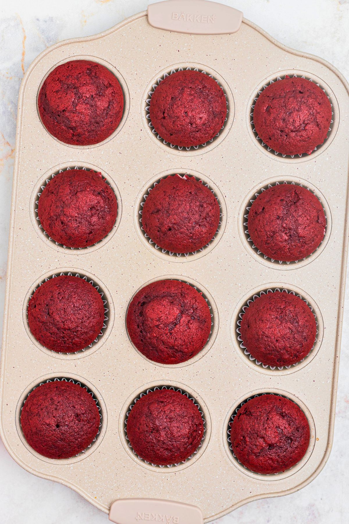 Bright red velvet cupcakes in a muffin tin after being baked.