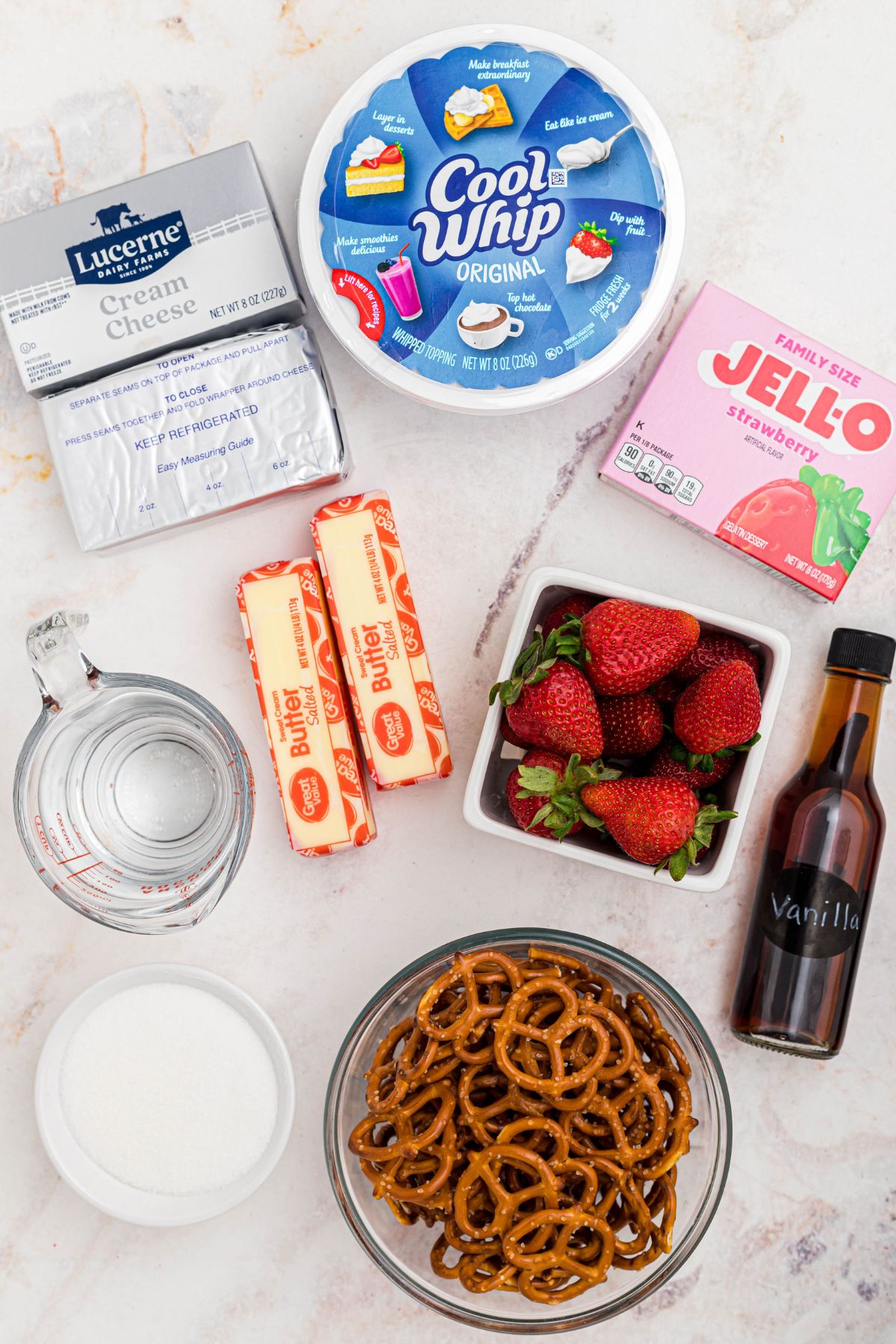 Ingredients needed to make strawberry pretzel salad measured in small bowls on a white marble table. 