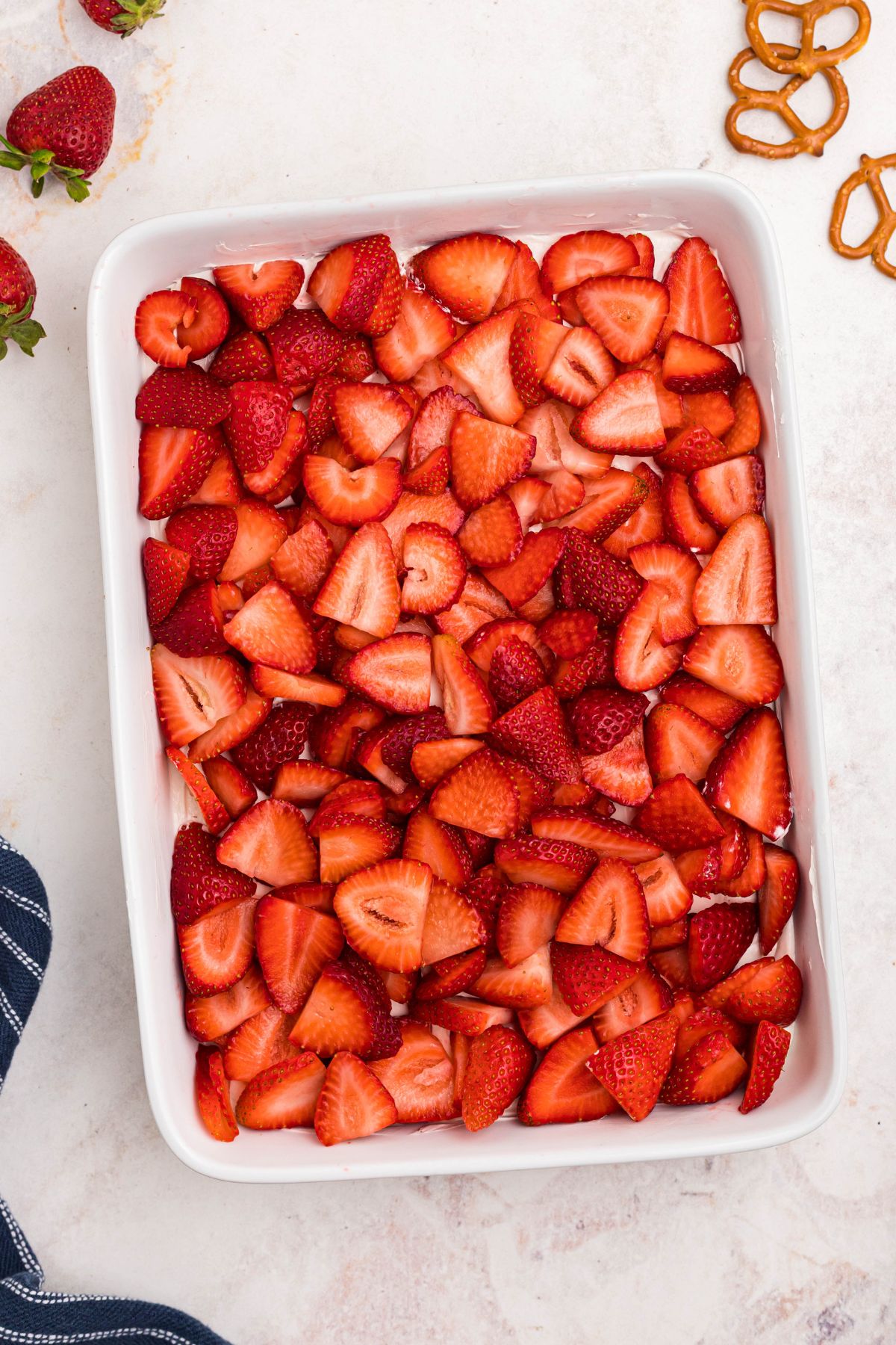 Strawberry slices spread over whipped topping in white baking dish.