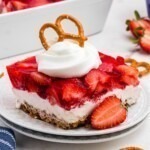 Layers of strawberry jello, pretzel crust and cream cheese filling, on a black plate.