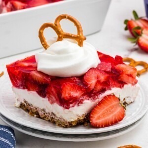 Layers of strawberry jello, pretzel crust and cream cheese filling, on a black plate.