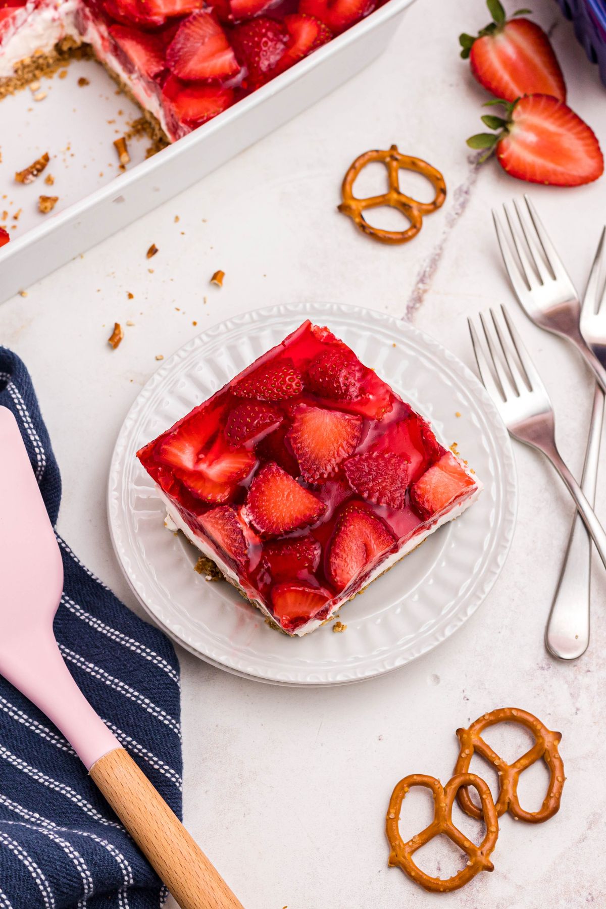 Slice of pretzel salad on small white plate with pink spatula next to plate.