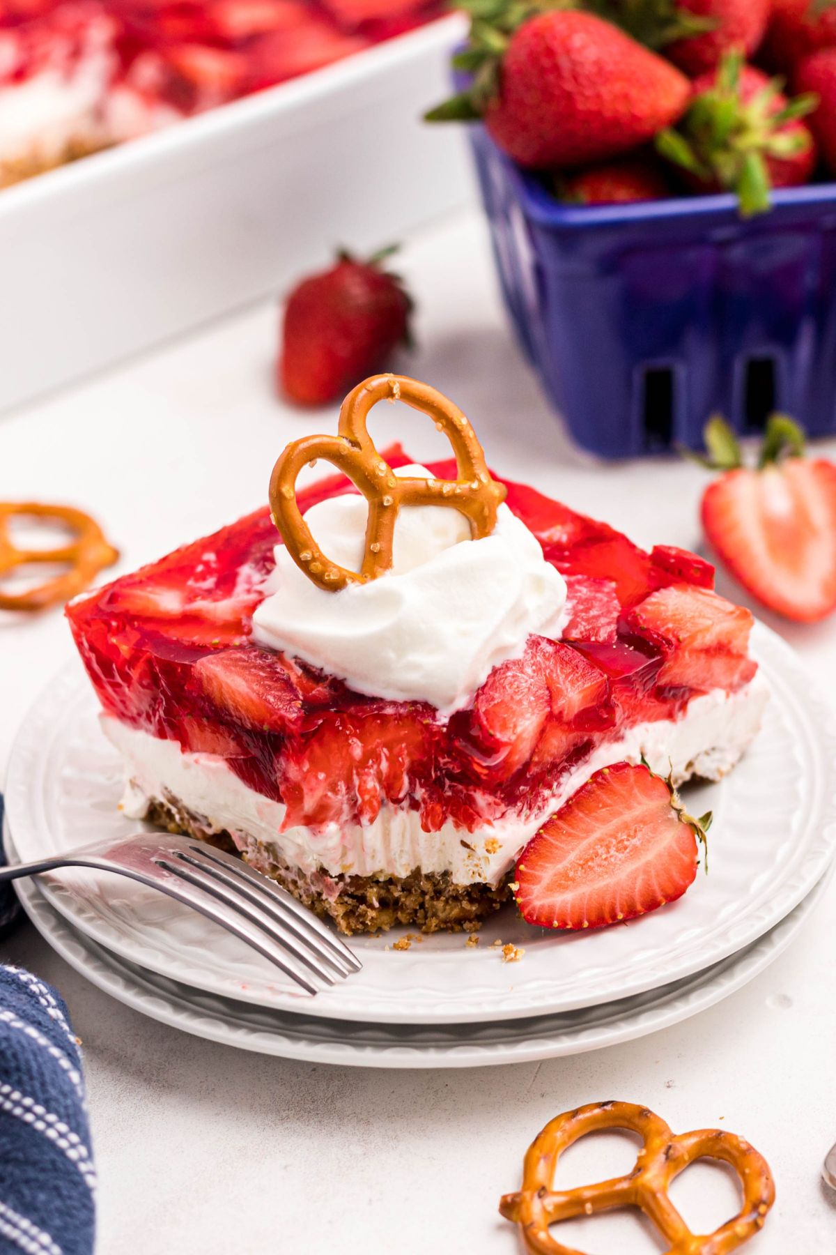 Slice of strawberry pretzel salad on small white plate with a fork on the side and a bite missing. 