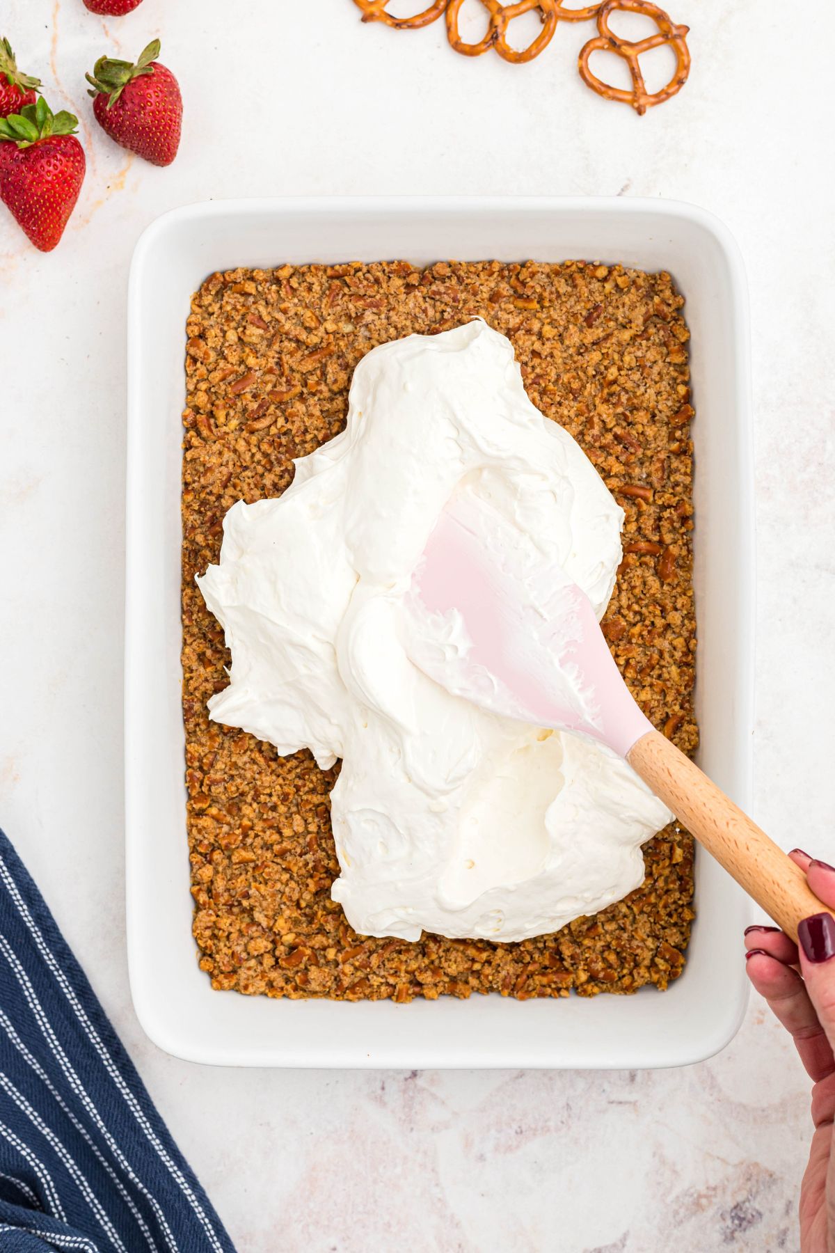 Whipped cream cheese topping being spread over pretzel crust.