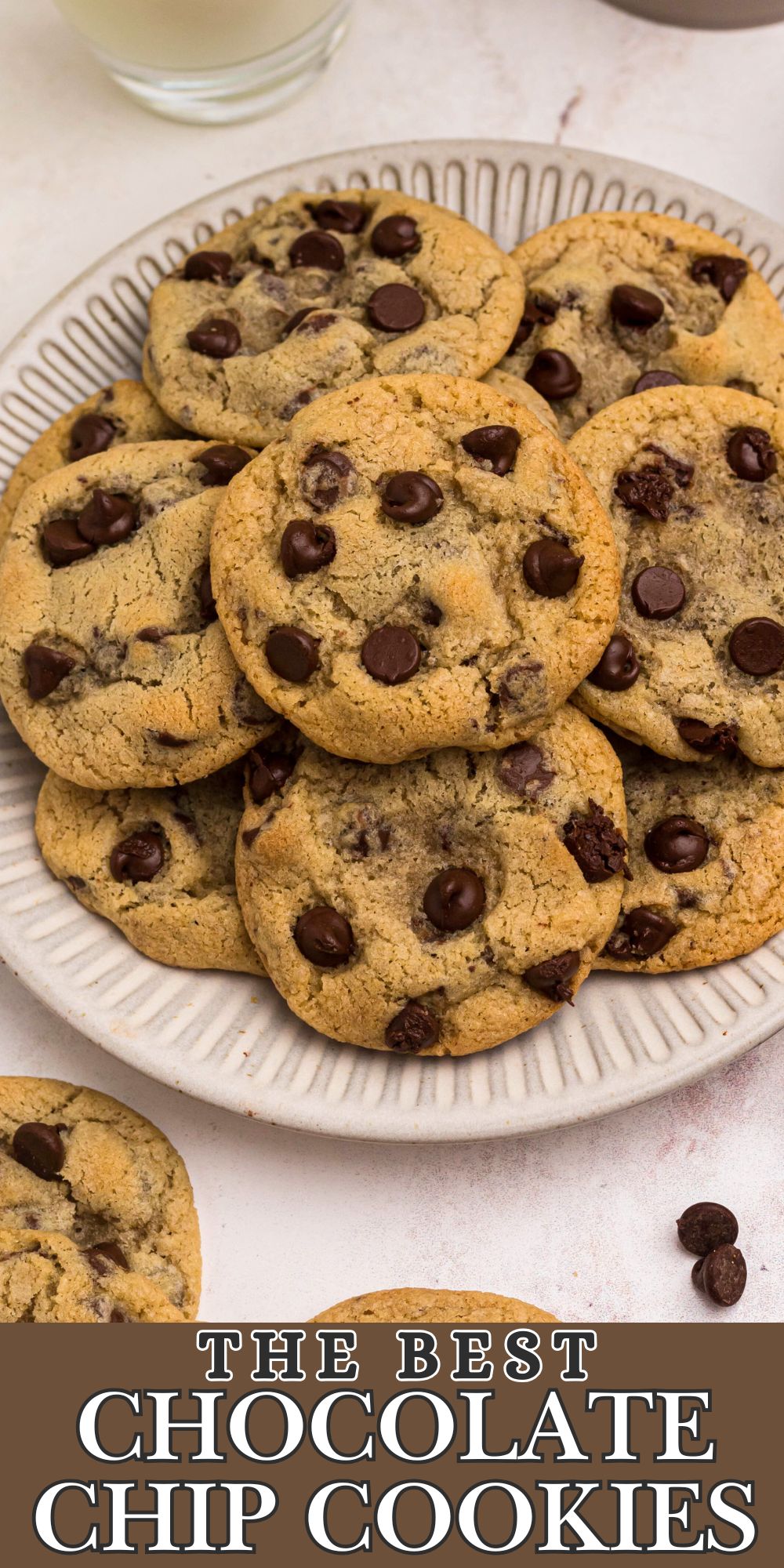 Chocolate chip cookies stacked on a white plate with chips and other cookies around them.