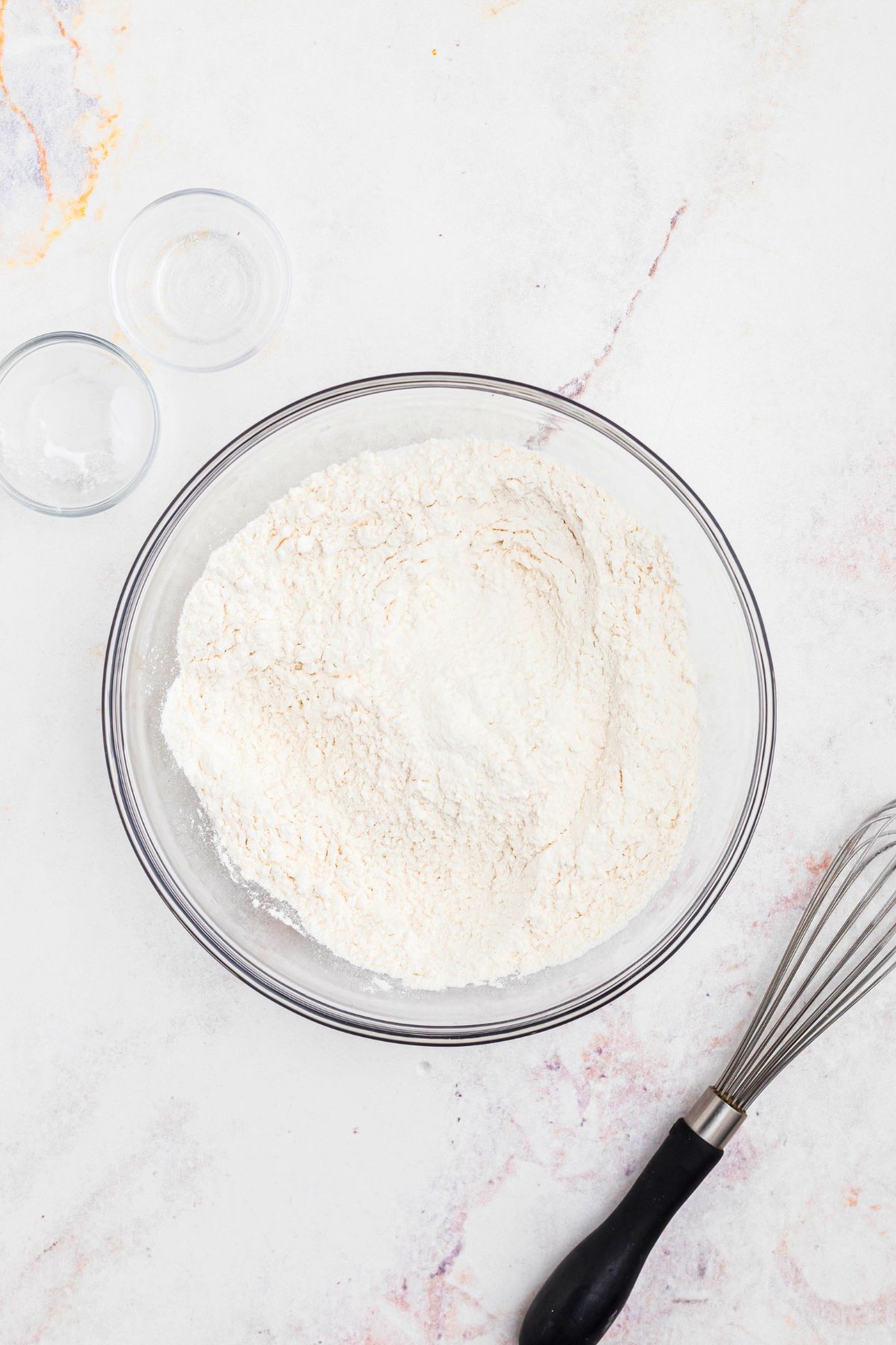 Flour and other dry ingredients mixed in a clear glass bowl. 