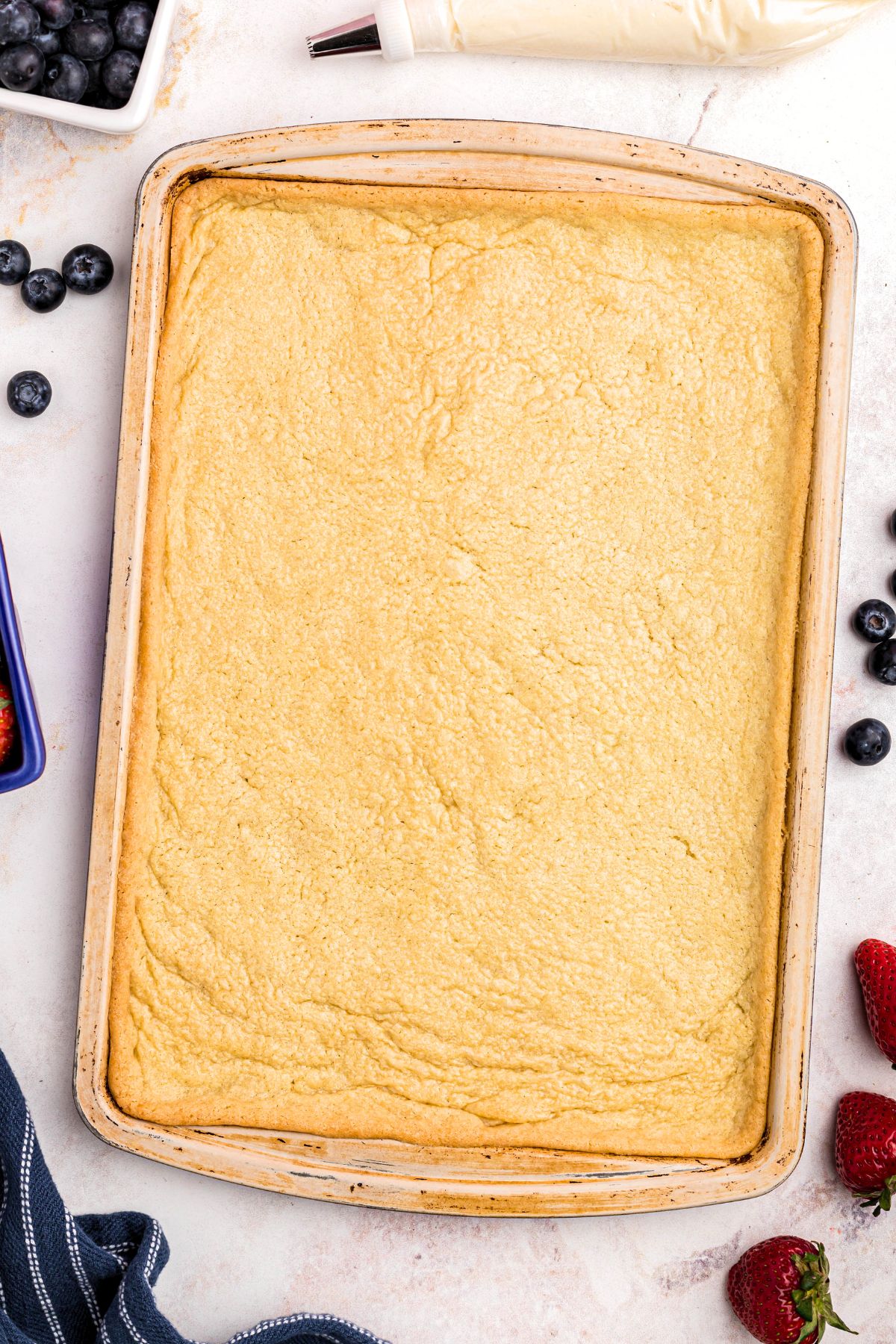 Sugar cookie baked into baking sheet with fresh fruit scattered around the table. 