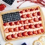 Rectangle cookie in cookie pan, topped with frosting, blueberries and strawberries, on a marble table.