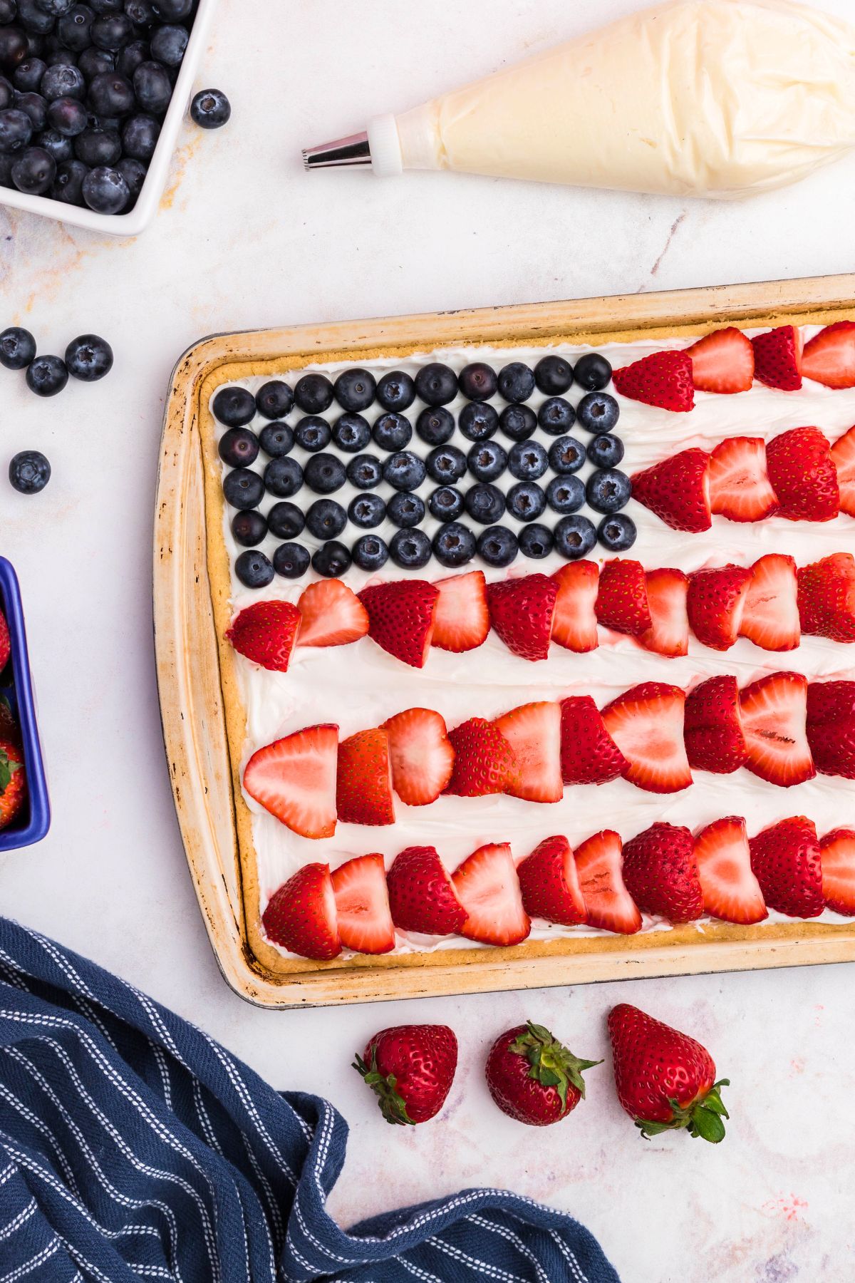 Fresh strawberry slices being added to frosted sugar cookie to resemble stripes on a flag. 