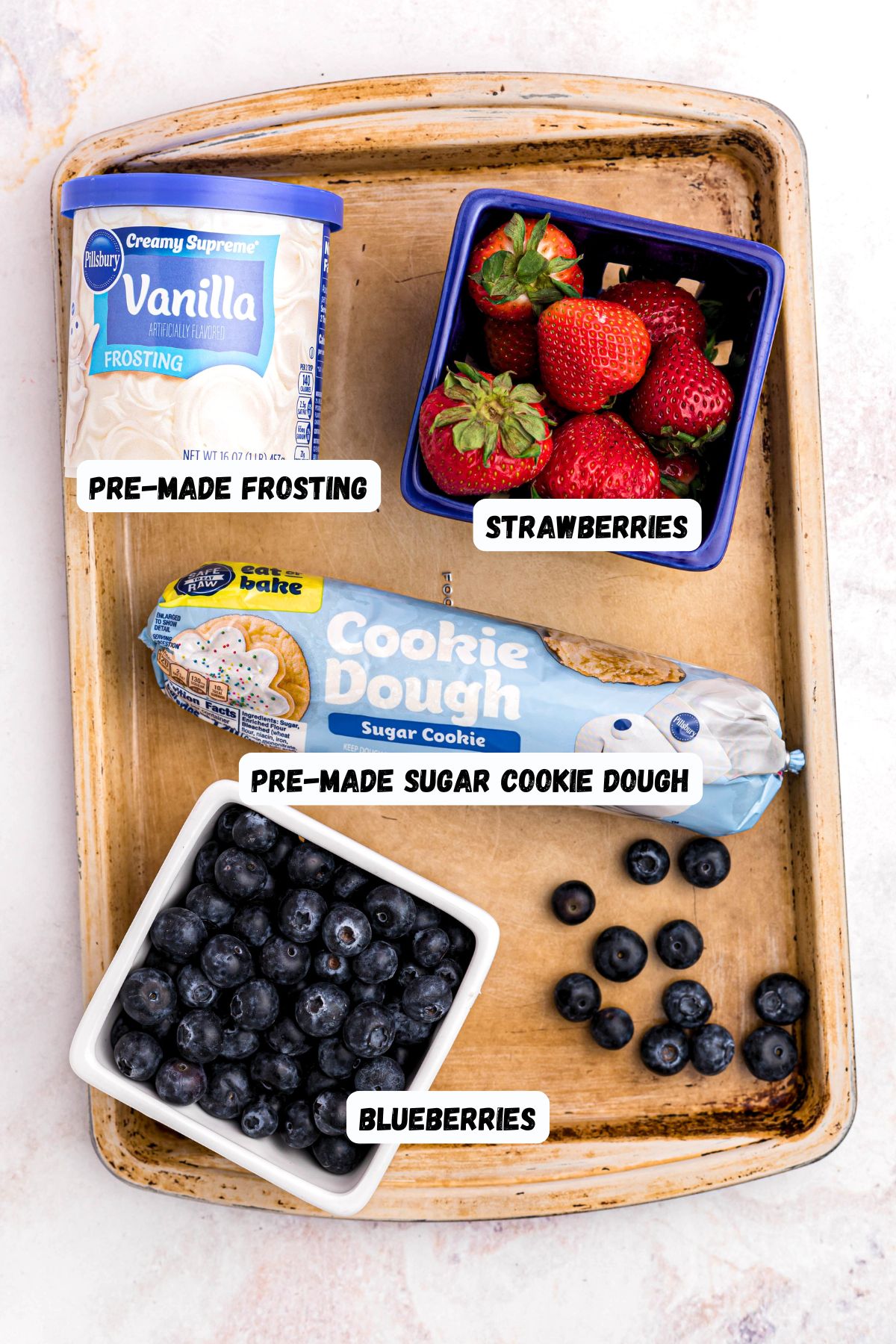 Cookie dough, frosting, and berries, on a baking sheet. 