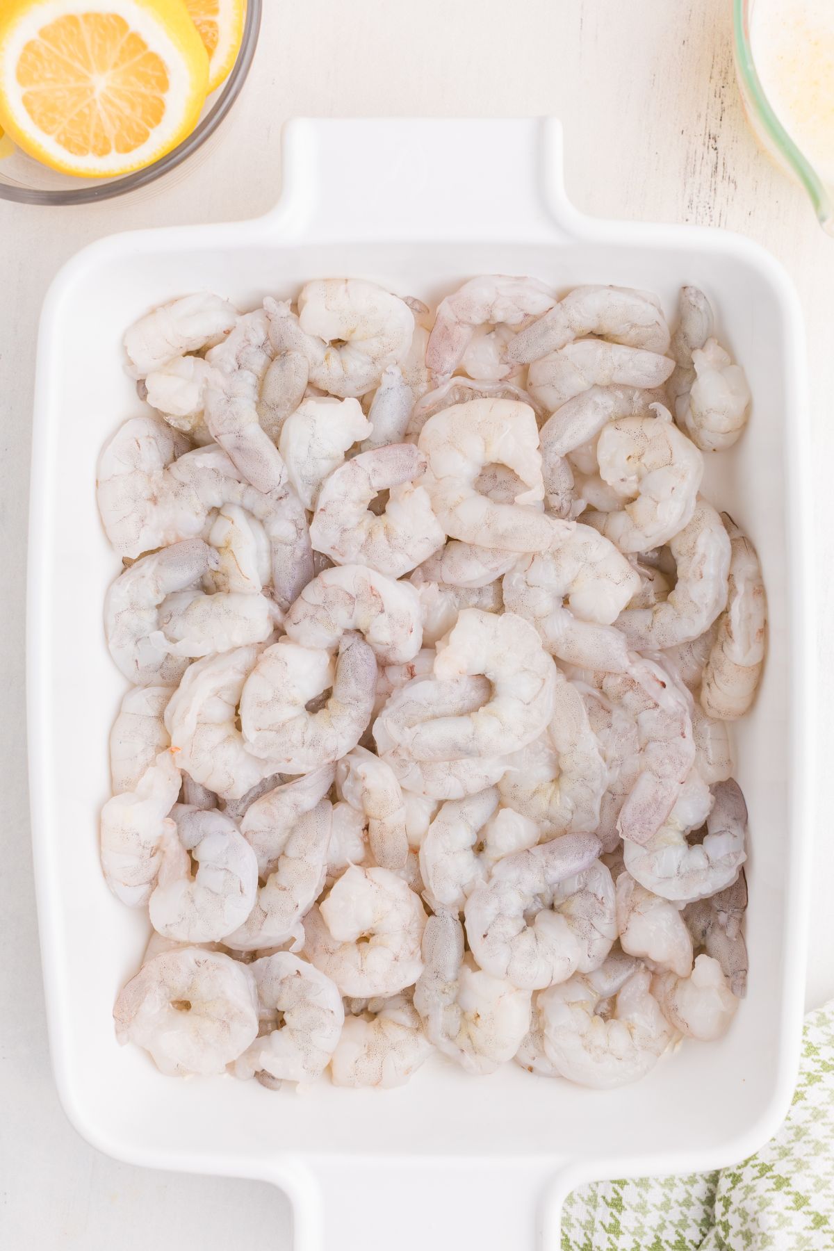 Uncooked shrimp in a white baking dish.