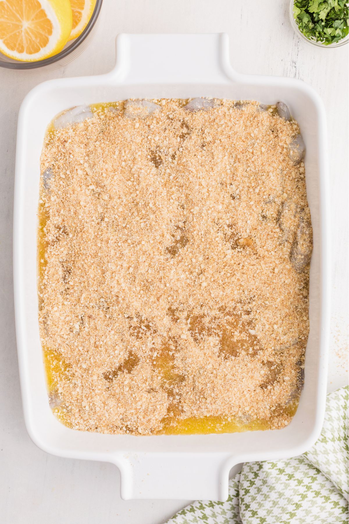 Shrimp topped with melted butter, seasonings, and breadcrumbs in a white baking dish.