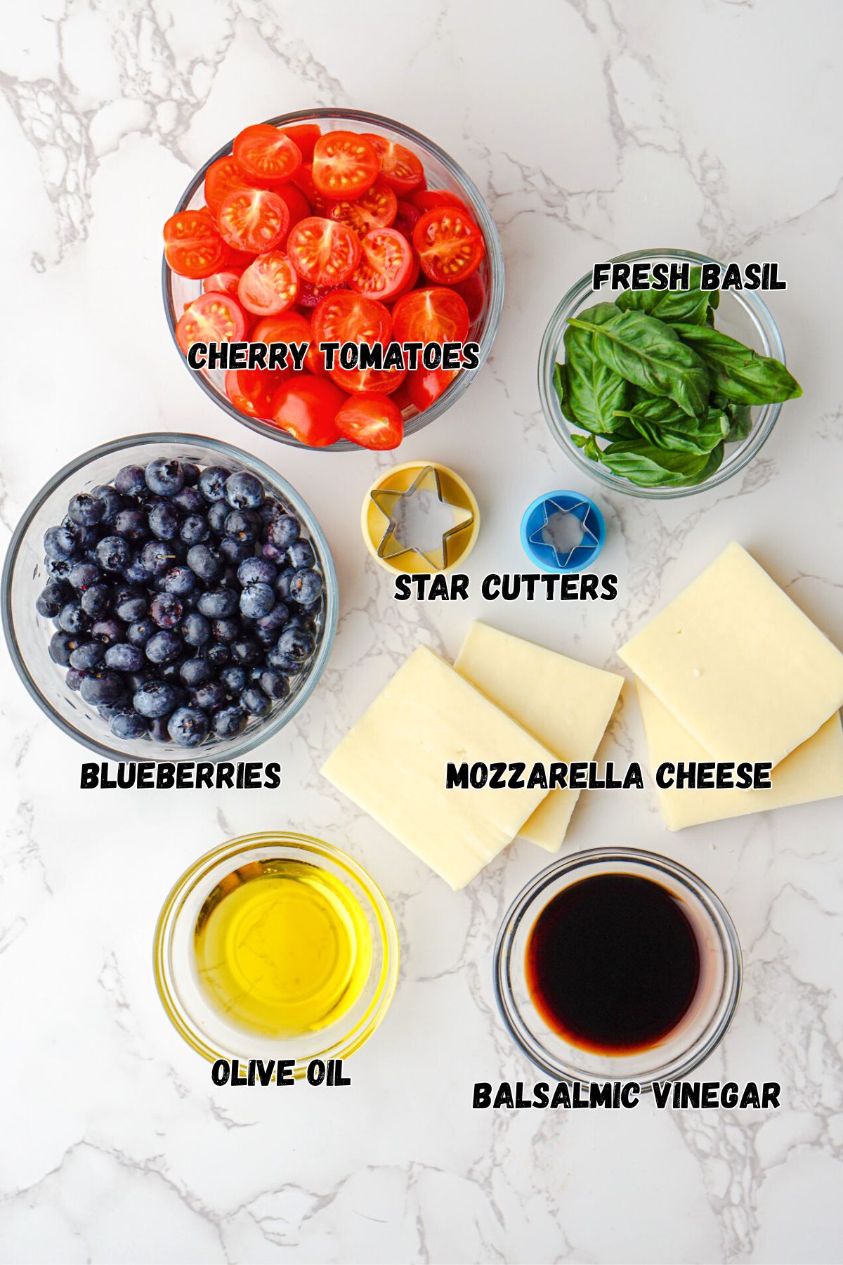 Ingredients needed to make Caprese salad, measured in small glass bowls on marble table. 