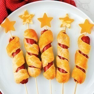 Five hot dogs wrapped in crescent roll dough, baked, and then topped with cheese stars, on a round white plate.