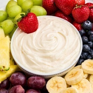 White bowl with fruit dip, surrounded by grapes, bananas, blueberries, and other fruits.