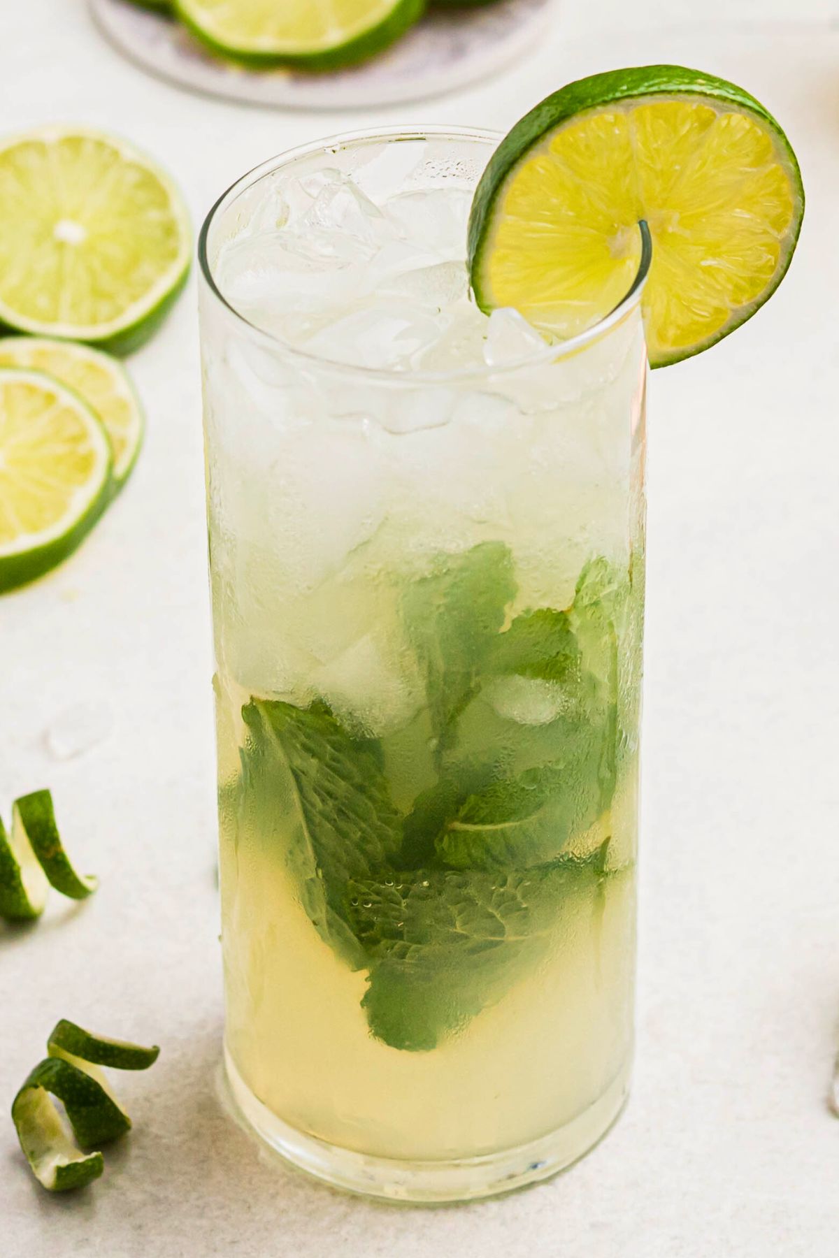 Bright yellow drink in a tall chilled glass, with limes and lime curls on the marble table.