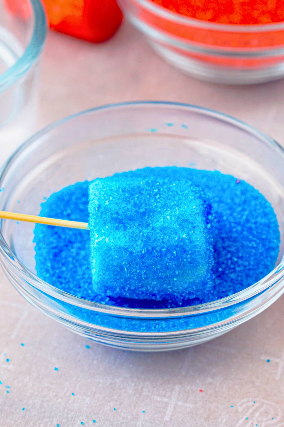 Marshmallow on toothpick being dipped in blue sugar.