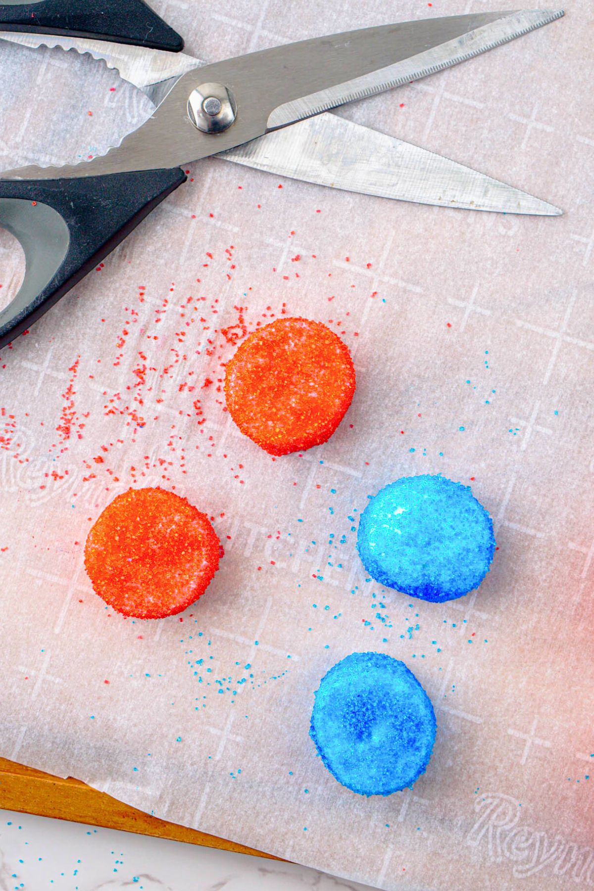 Red and blue sugar coated marshmallows being cut in half with kitchen shears.
