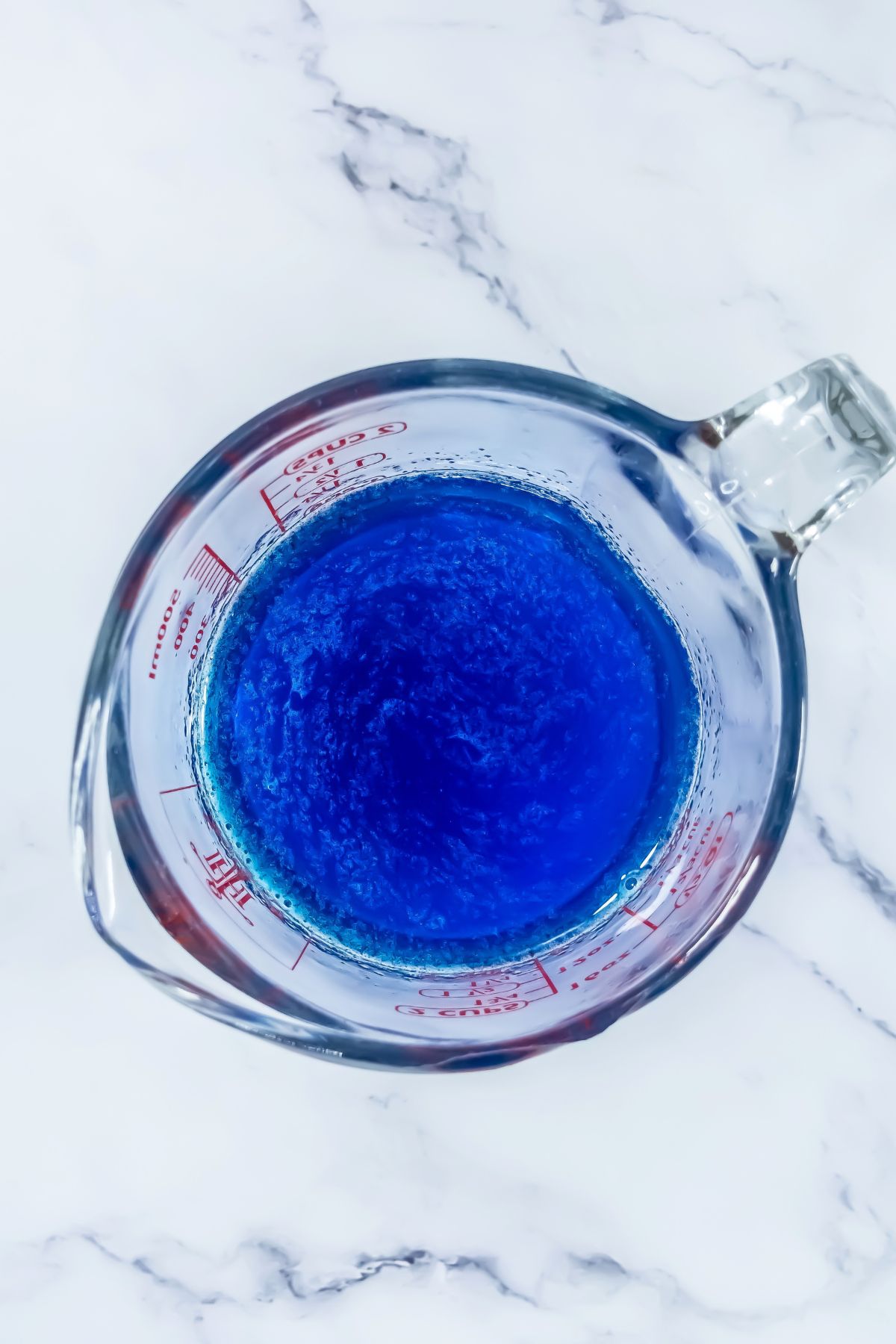 Blue powder and vodka mixed together in a clear glass bowl on a marble table. 
