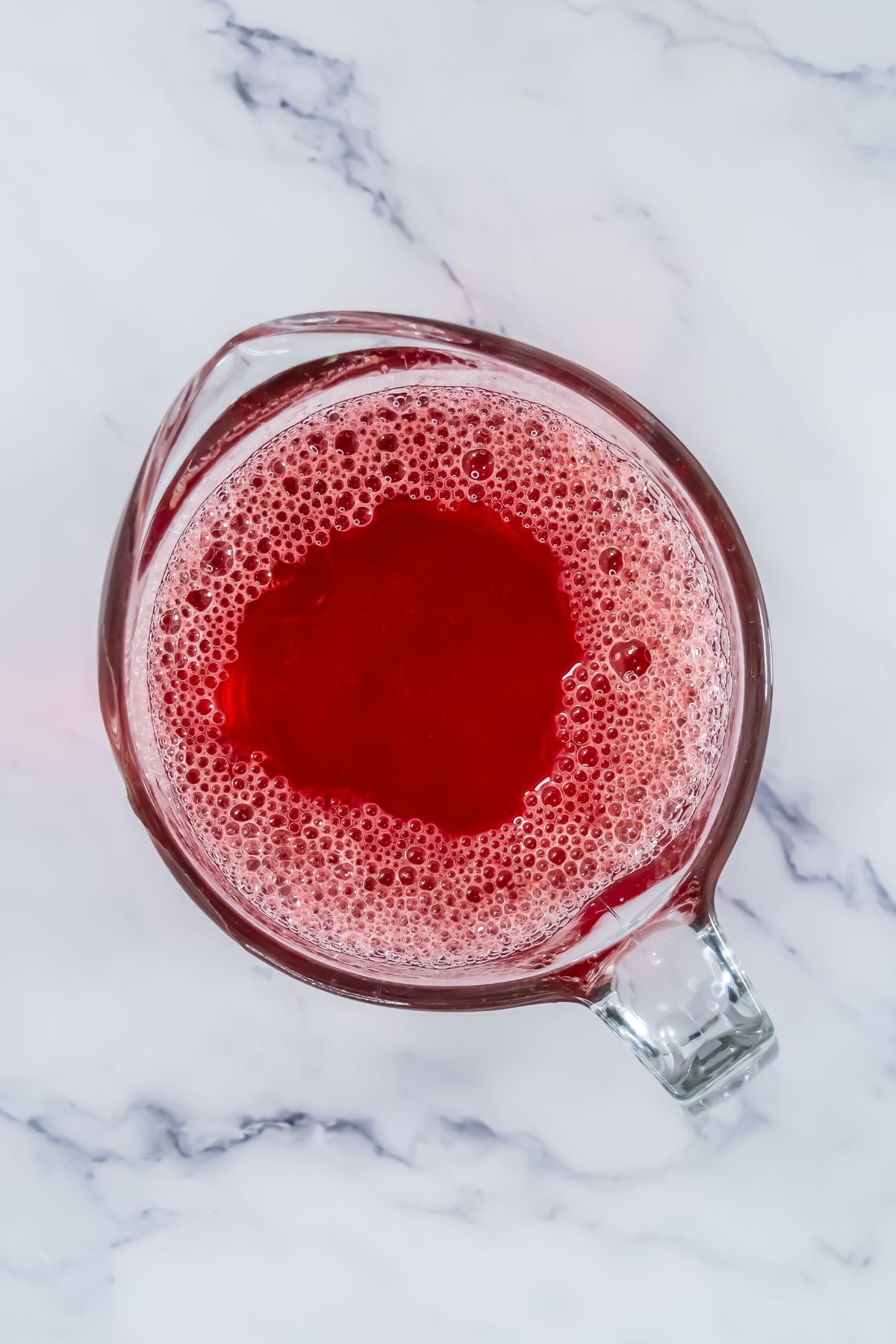 Red powder mixed with water and vodka in a clear glass measuring cup on a white marble table. 