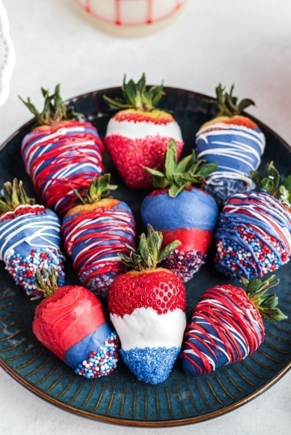 Red, white, and blue, dipped strawberries, placed side by side n a dark blue plate.