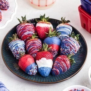 Red, white, and blue, dipped strawberries, placed side by side n a dark blue plate.