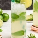 Bright yellow drink in a tall chilled glass, with limes and lime curls on the marble table.