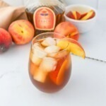 Glass filled with ice, peach whiskey, and tea, on a white marble table.