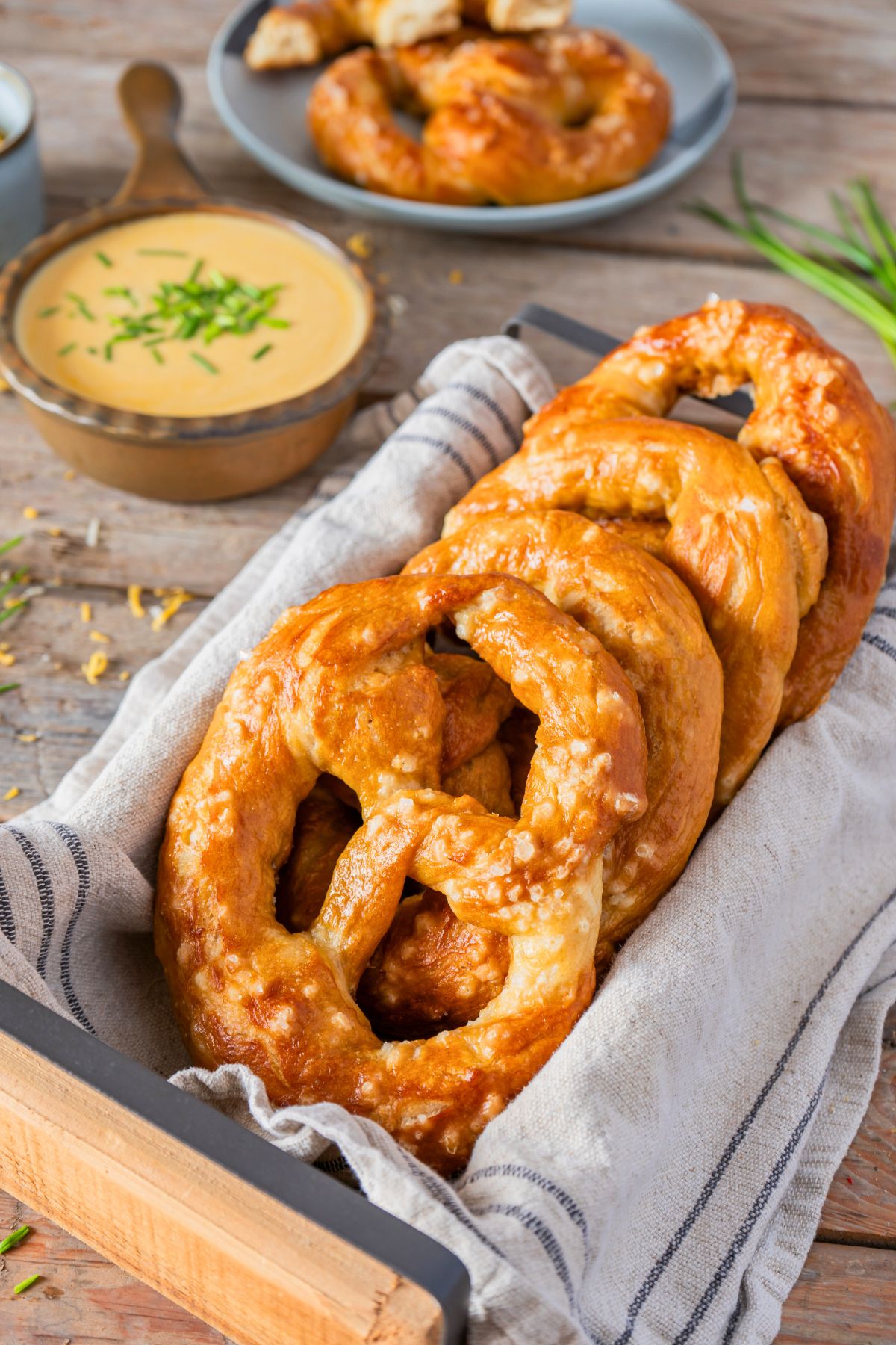Golden baked soft pretzels stacked in a bread box, in front of cheese dip. 