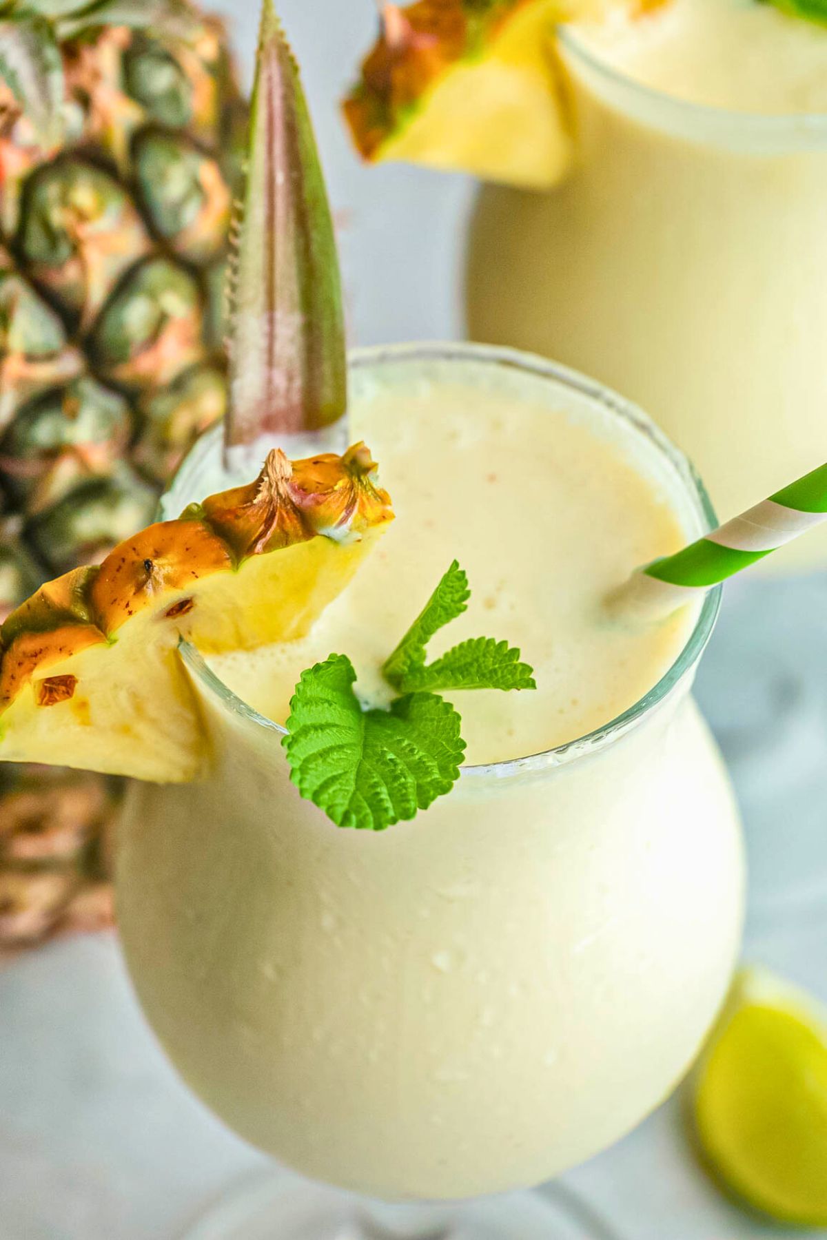 Frozen blended drink in a frosted glass, garnished with pineapple wedge and a green straw. 
