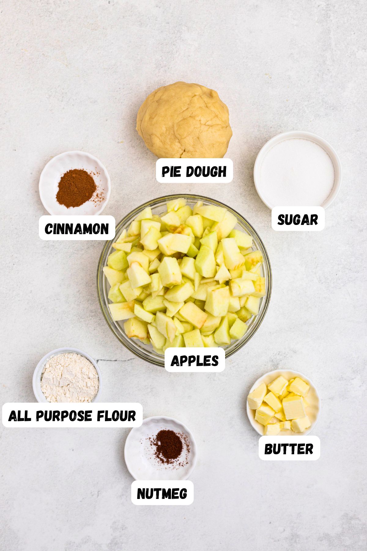 Ingredients needed to make apple pie, measured into small bowls, on a white marble table. 