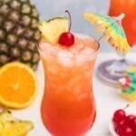 Red and orange drink mixed together, with a paper umbrella, in a hurricane glass with orange slices and cherries on the marble table.