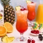 Red and orange drink mixed together in a hurricane glass with orange slices and cherries on the marble table.