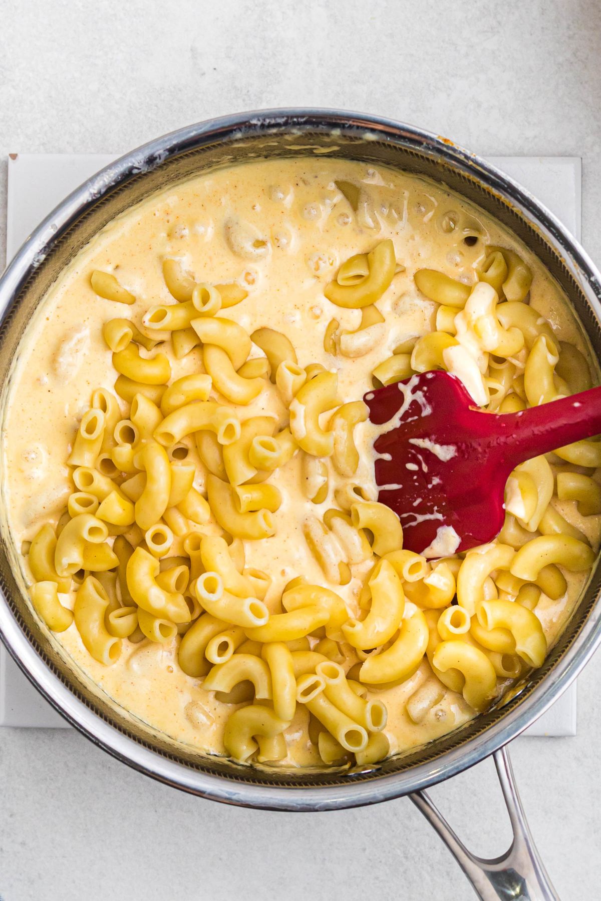 Melted cheese being mixed with elbow macaroni in a saucepan.