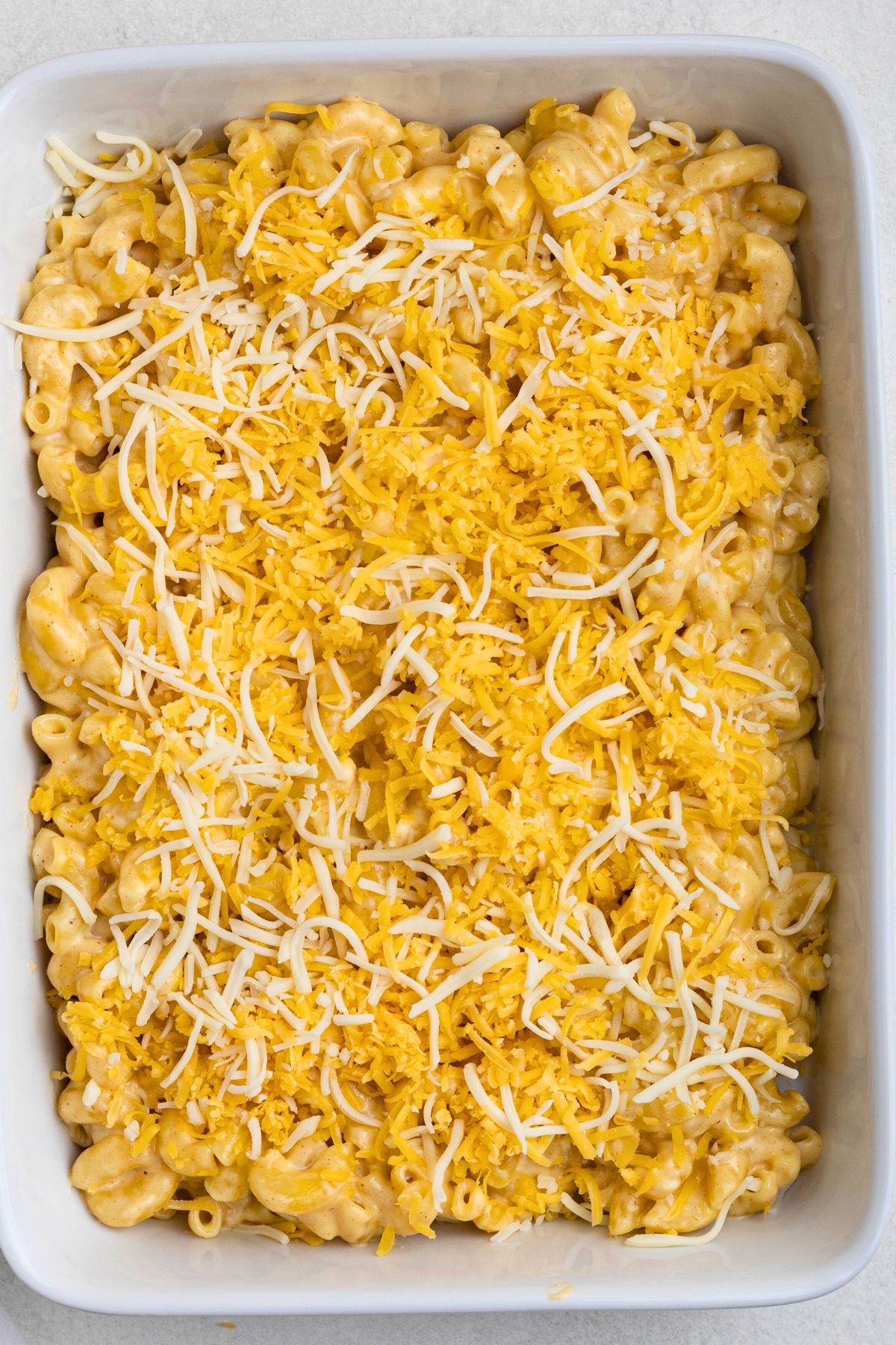 Mac and cheese in a baking dish, topped with shredded cheeses, before baking.