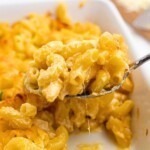 Spoonful of mac and cheese being lifted out of casserole dish.