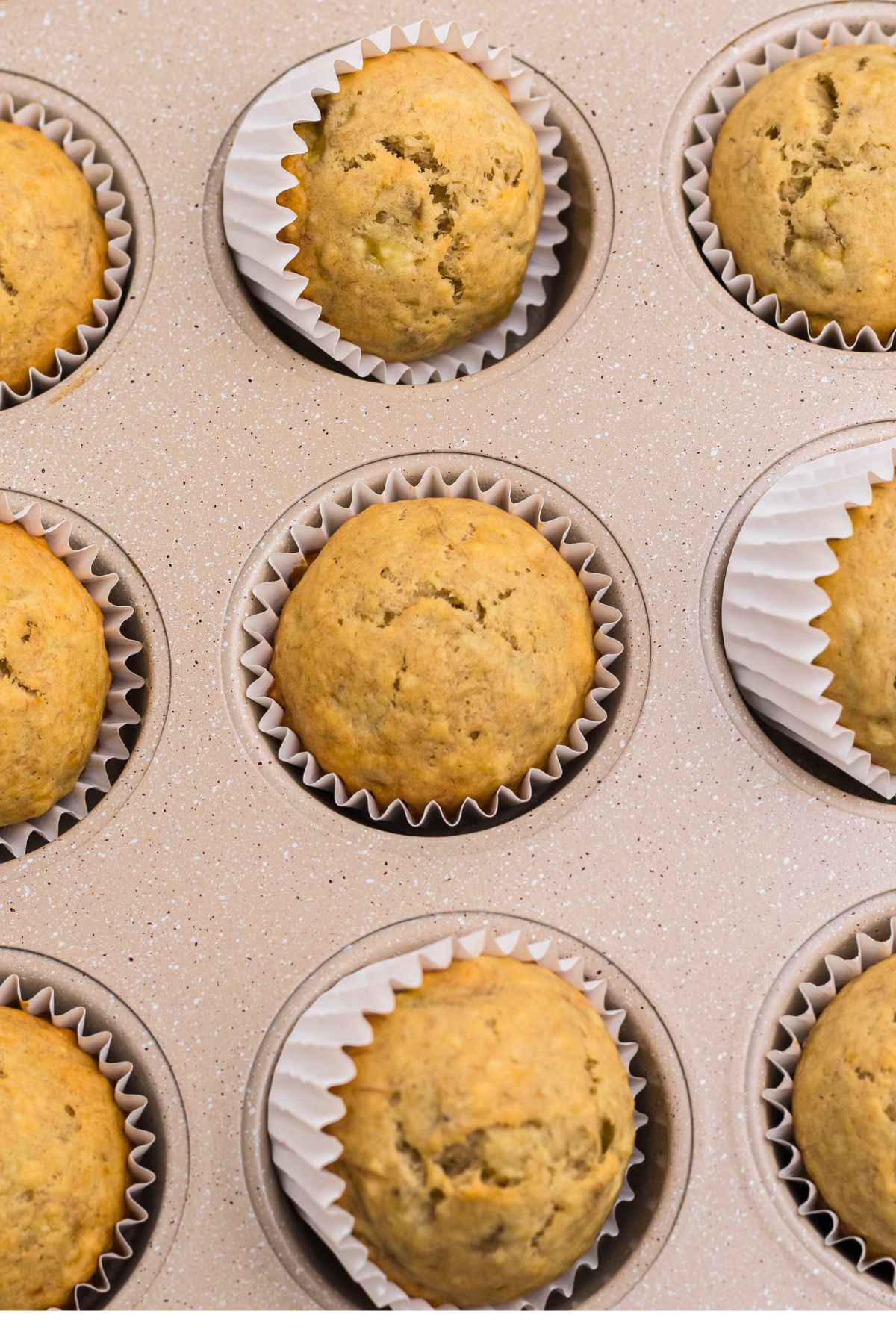 Baked muffins in a muffin pan on a marble table.
